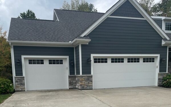 Two white, short-paneled garage doors with windows against a blue house.